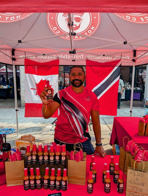 Salesperson holds up bottle of hot sauce behind the person are two flags